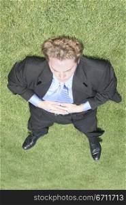 Businessman wearing black suit and blue shirt is completely sprawled out on the green grass