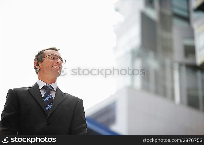 Businessman wearing earphone standing outside building low angle view