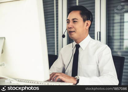 Businessman wearing headset working actively in office . Call center, telemarketing, customer support agent provide service on telephone video conference call.. Businessman wearing headset working actively in office