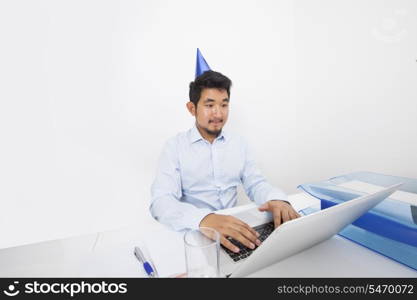 Businessman wearing party hat while using laptop in office