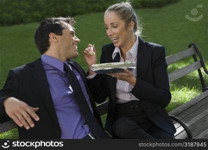 Businessman with a businesswoman having food on a park bench
