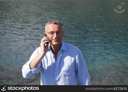 Businessman with a cellphone in front of water