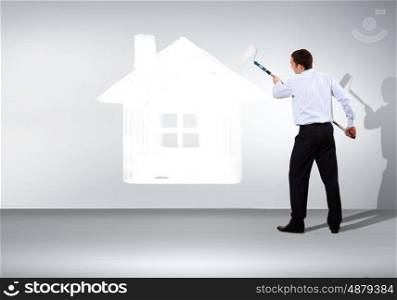 Businessman with a paint brush and picture of house on the wall
