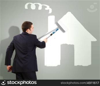 Businessman with a paint brush and picture of house on the wall