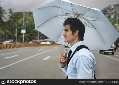 Businessman with an umbrella crossing a road