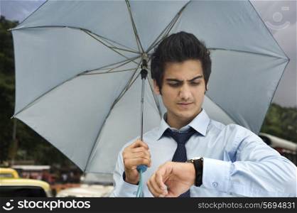 Businessman with an umbrella looking at his watch