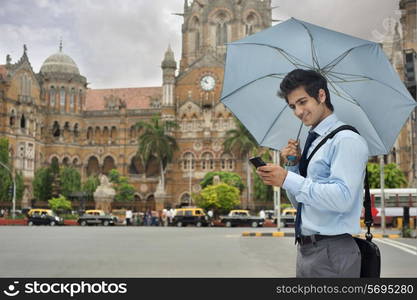 Businessman with an umbrella reading an sms