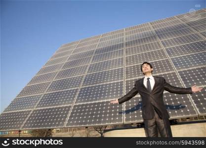 Businessman with arms outstretched in front of solar panels