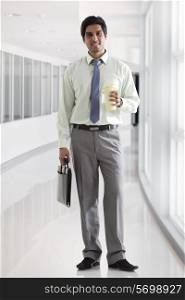 Businessman with bag and coffee cup standing in office corridor