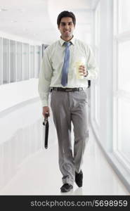 Businessman with bag and coffee cup walking in office corridor