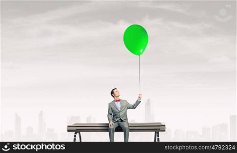 Businessman with balloon. Young businessperson sitting on a wooden bench and relaxing