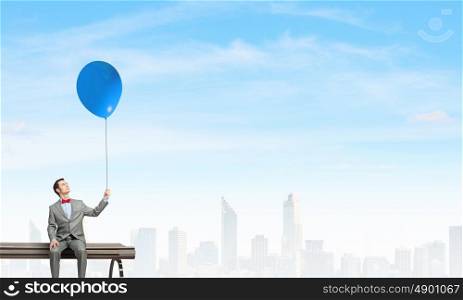 Businessman with balloon. Young businessperson sitting on a wooden bench and relaxing