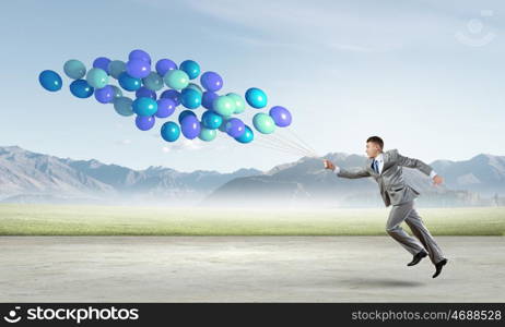 Businessman with balloons. Cheerful businessman running with bunch of colorful balloons