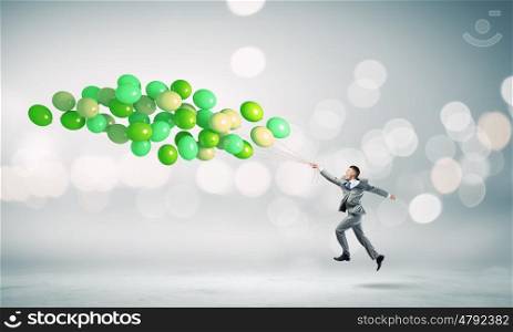 Businessman with balloons. Cheerful businessman running with bunch of colorful balloons