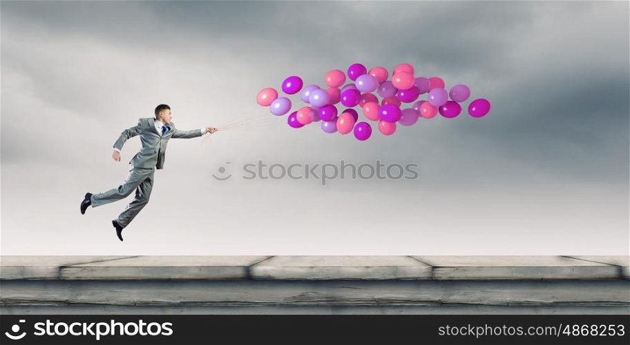 Businessman with balloons. Cheerful businessman running with bunch of colorful balloons