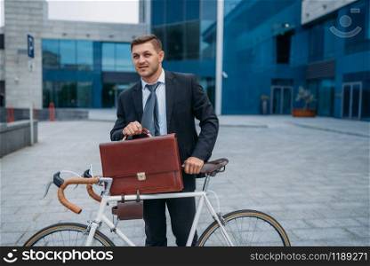 Businessman with bicycle near office building in downtown. Business person riding on eco transport on city street