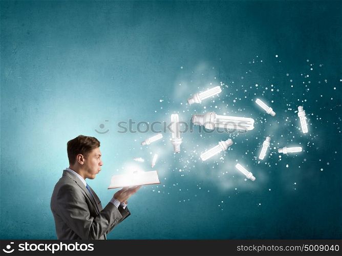 Businessman with book in hands. Businessman holding opened book with glass glowing light bulb
