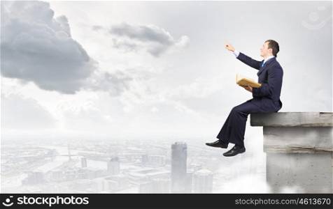 Businessman with book. Young businessman reading book sitting on roof of building