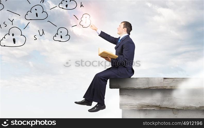 Businessman with book. Young businessman reading book sitting on roof of building