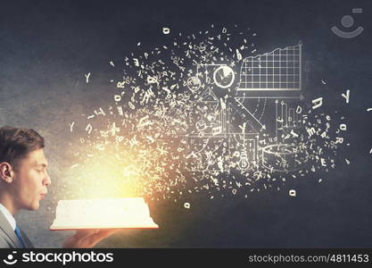 Businessman with book. Young businessman with opened book in hands blowing on pages