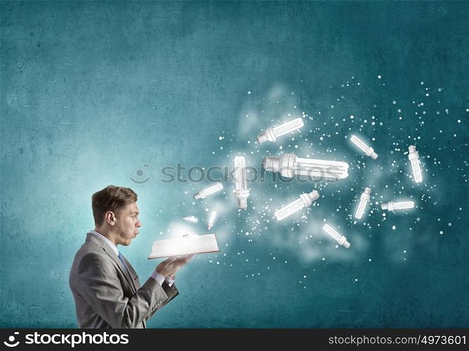 Businessman with book. Young businessman with opened book in hands blowing on pages