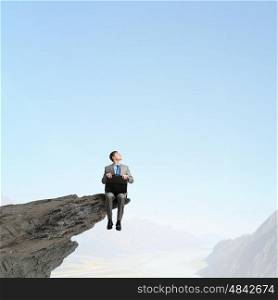 Businessman with briefcase. Businessman with briefcase in hands sitting on rock top