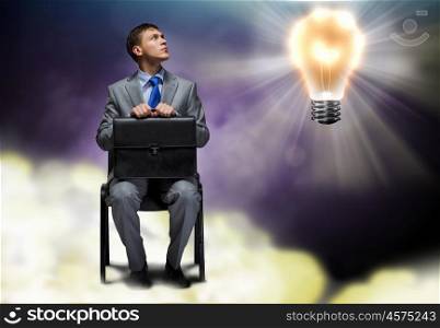 Businessman with briefcase. Young businessman sitting on chair with briefcase in hands