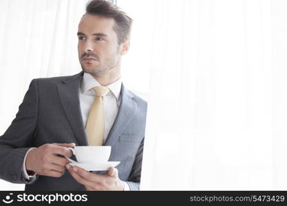 Businessman with coffee cup looking away in office