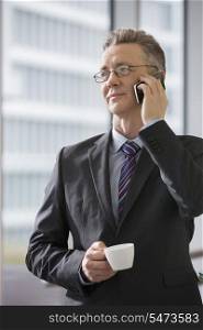 Businessman with coffee cup using cell phone in office
