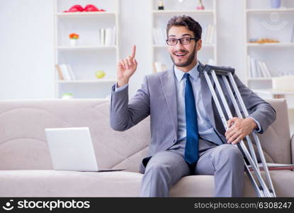 Businessman with crutches and broken leg at home working