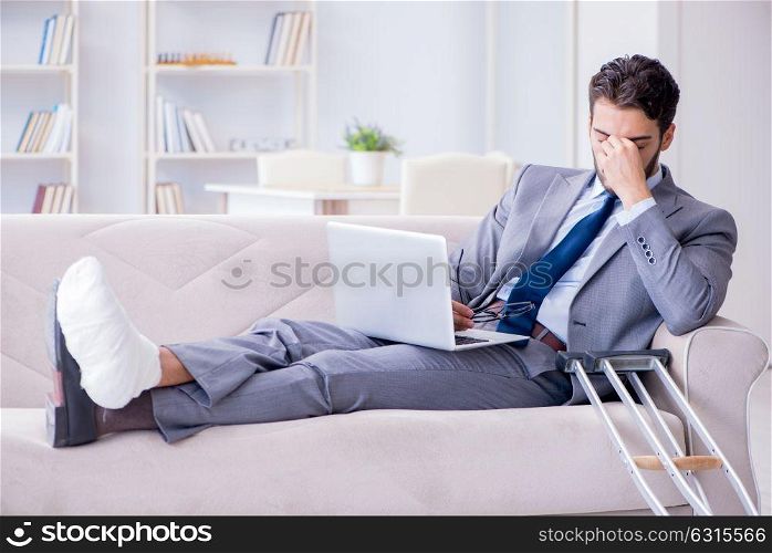 Businessman with crutches and broken leg at home working