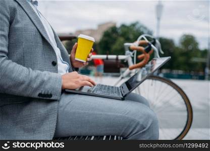 Businessman with cycle drinks coffee on the bench at the office building in downtown. Business person riding on eco transport on city street, urban style