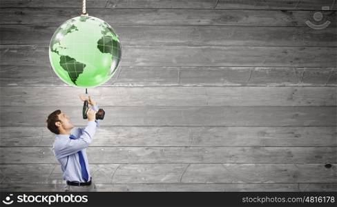 Businessman with drill. Young businessman tighten screw in to planet with drill
