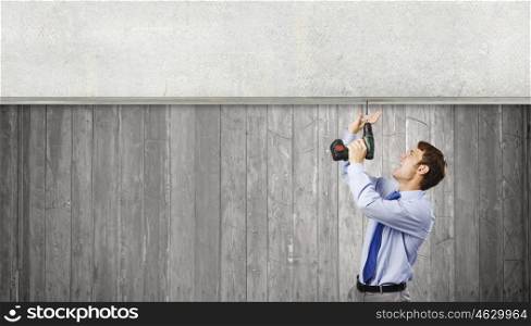 Businessman with drill. Young businessman using drill to fix banner