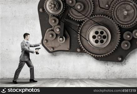 Businessman with drill. Young businessman using drill to fix gear mechanism