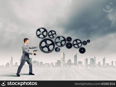 Businessman with drill. Young businessman using drill to fix gear mechanism