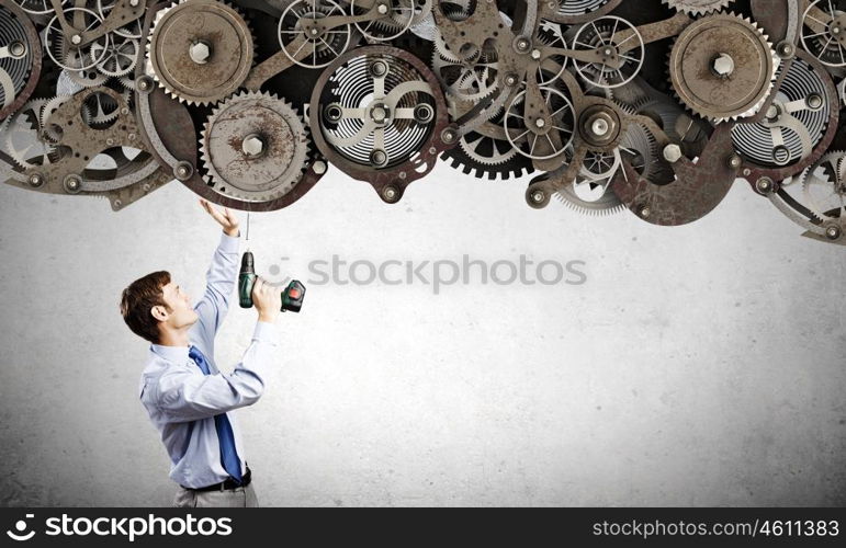 Businessman with drill. Young businessman using drill to fix gear mechanism