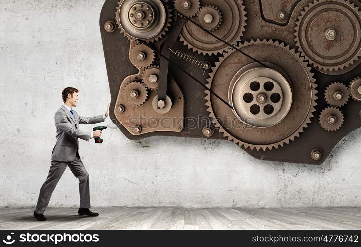 Businessman with drill. Young businessman using drill to fix gear mechanism