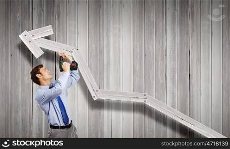 Businessman with drill. Young businessman using drill to fix growing arrow