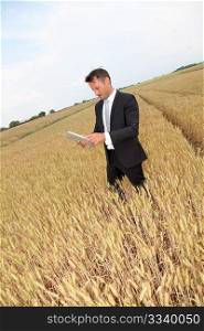 Businessman with electronic tablet standing in wheat field