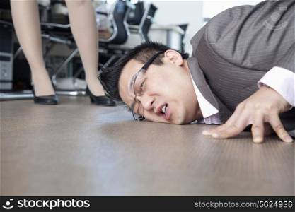 Businessman with face on the floor, coworker standing by him