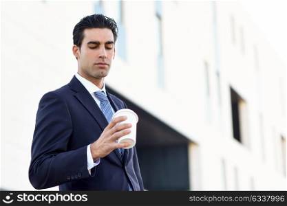 Businessman with formal clothes drinking coffee to go with a take away cup. Man wearing blue suit and tie in urban background.