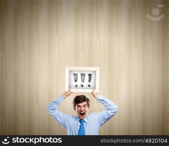 Businessman with frame. Young anxious businessman holding frame with exclamation marks