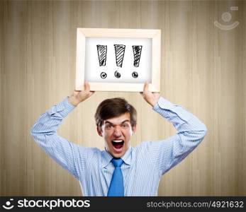 Businessman with frame. Young anxious businessman holding frame with exclamation marks