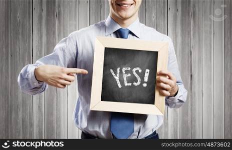 Businessman with frame. Young smiling businessman holding chalkboard with yes word