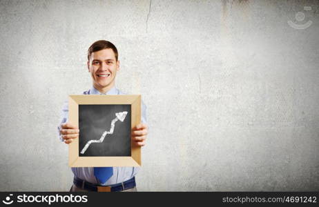 Businessman with frame. Young smiling businessman holding wooden frame with graph