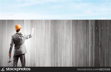 Businessman with hammer. Rear view of businessman hammering nail in fence