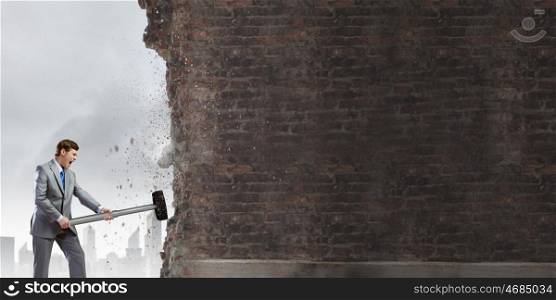 Businessman with hammer. Young determined businessman with big hammer in hands crashing wall