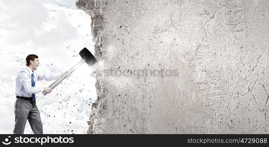 Businessman with hammer. Young determined businessman with big hammer in hands crashing wall