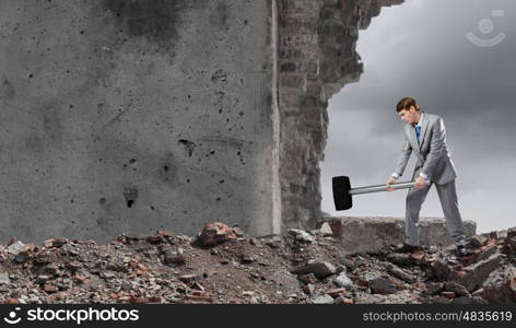 Businessman with hammer. Young determined businessman with big hammer in hands crashing wall